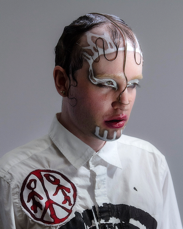 Jesse Clark with white veiny facepaint and slicked hair against a white background.
